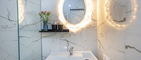 A bathroom with a white sink, a mirror with a light halo, and a vase with flowers.