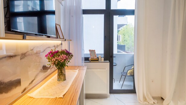 Una cocina moderna con encimera de madera, un jarrón de flores, un televisor montado sobre la encimera y vistas al balcón exterior.
