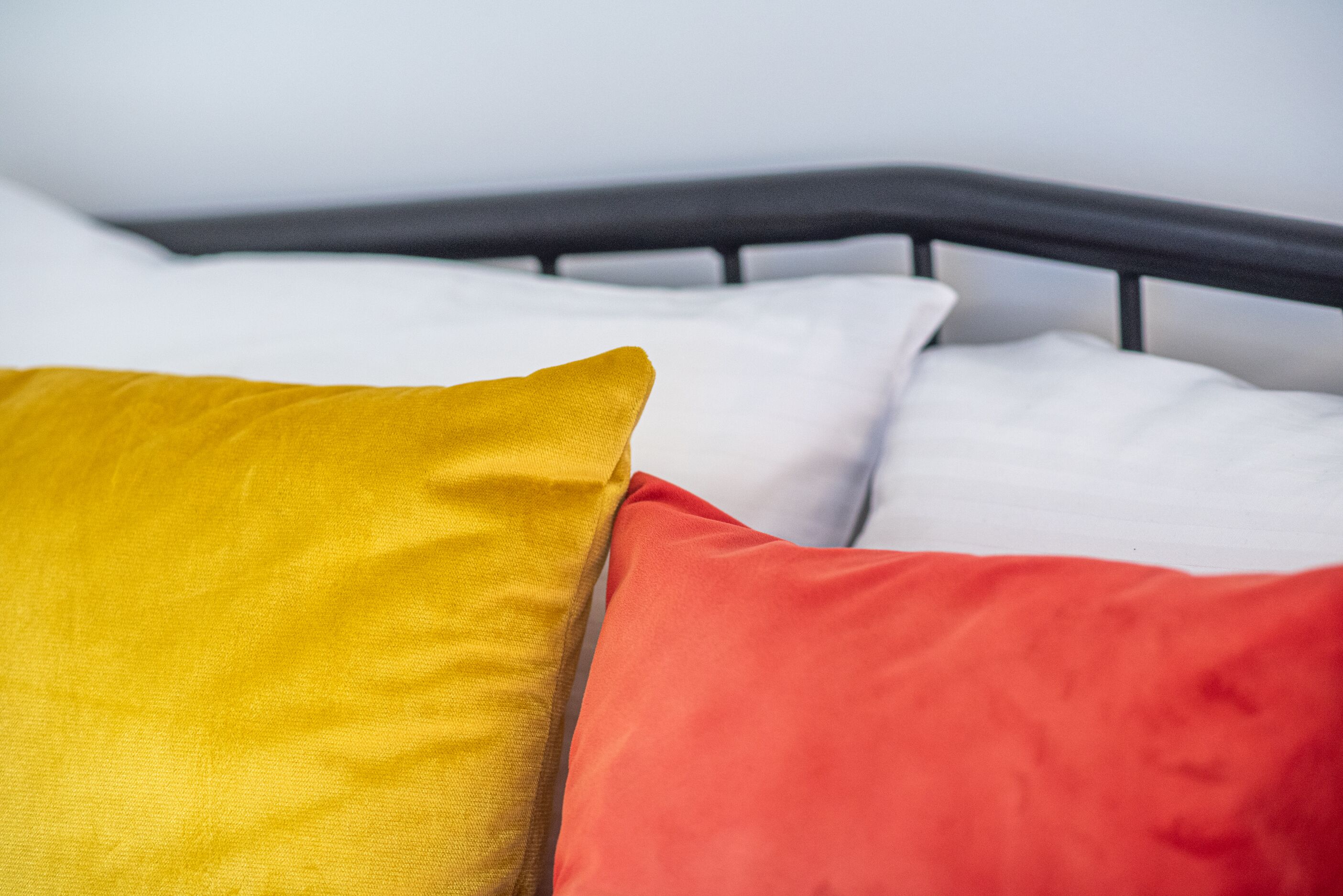 Cama com estrutura metálica preta e almofadas em amarelo e vermelho.