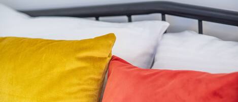Cama com estrutura metálica preta e almofadas em amarelo e vermelho.