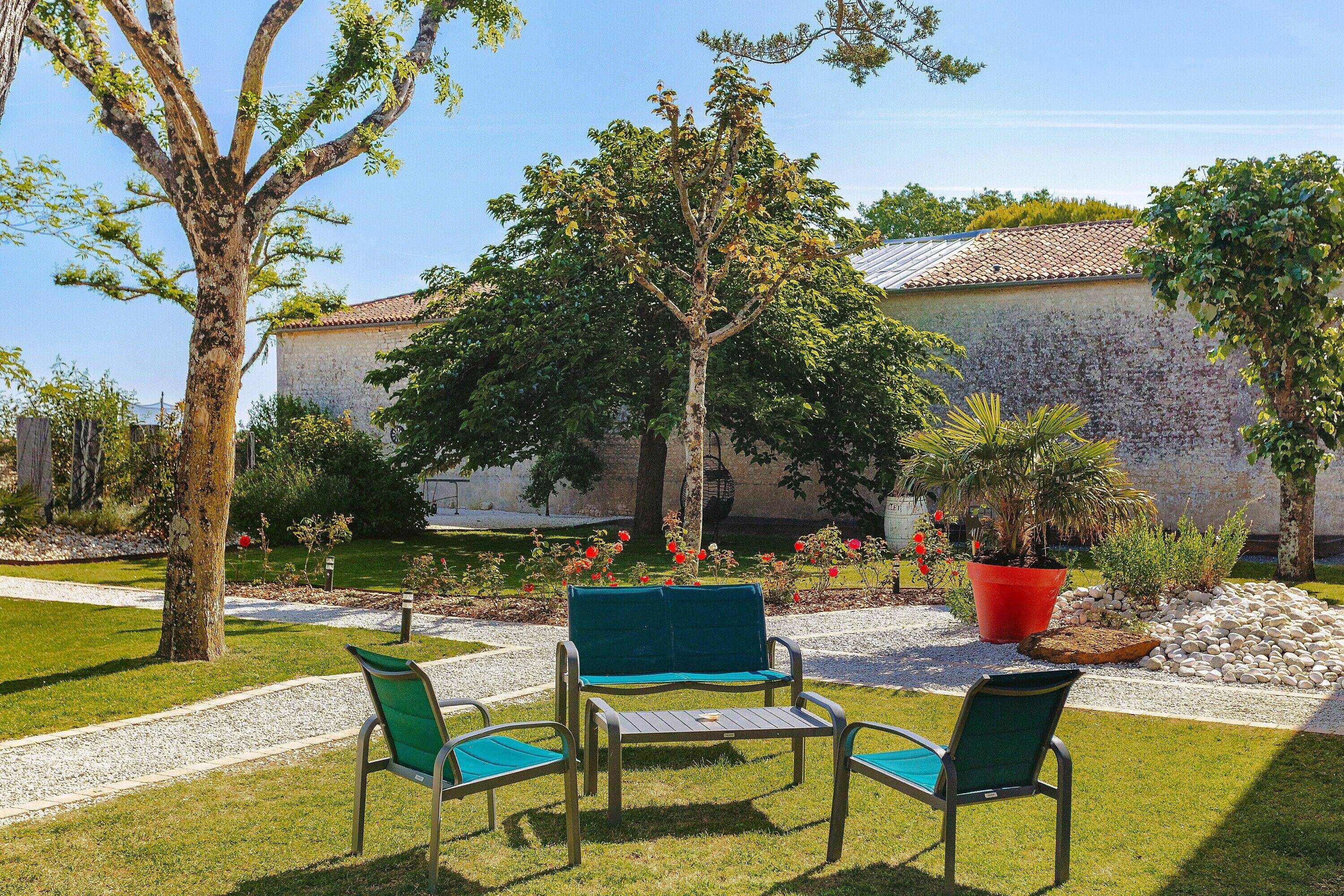 A patio with a table and chairs, surrounded by a garden with trees and potted plants.