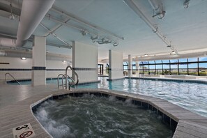 Ein Hallenbad mit Whirlbereich, transparenter Decke und sichtbaren Rohren, mit Blick ins Freie durch große Fenster.