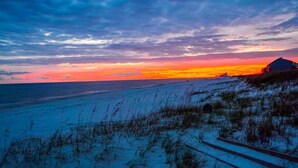 A beach scene with a sunset, a dune, and a building. - Emerald by the Sea at Lost Key Golf & Beach Club | Resort Amenities | Beach Shuttle | Beach Getaways (Pensacola)
