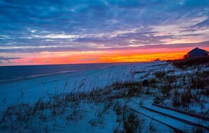 A beach scene with a sunset, a dune, and a building. - Emerald by the Sea at Lost Key Golf & Beach Club | Resort Amenities | Beach Shuttle | Beach Getaways (Pensacola)