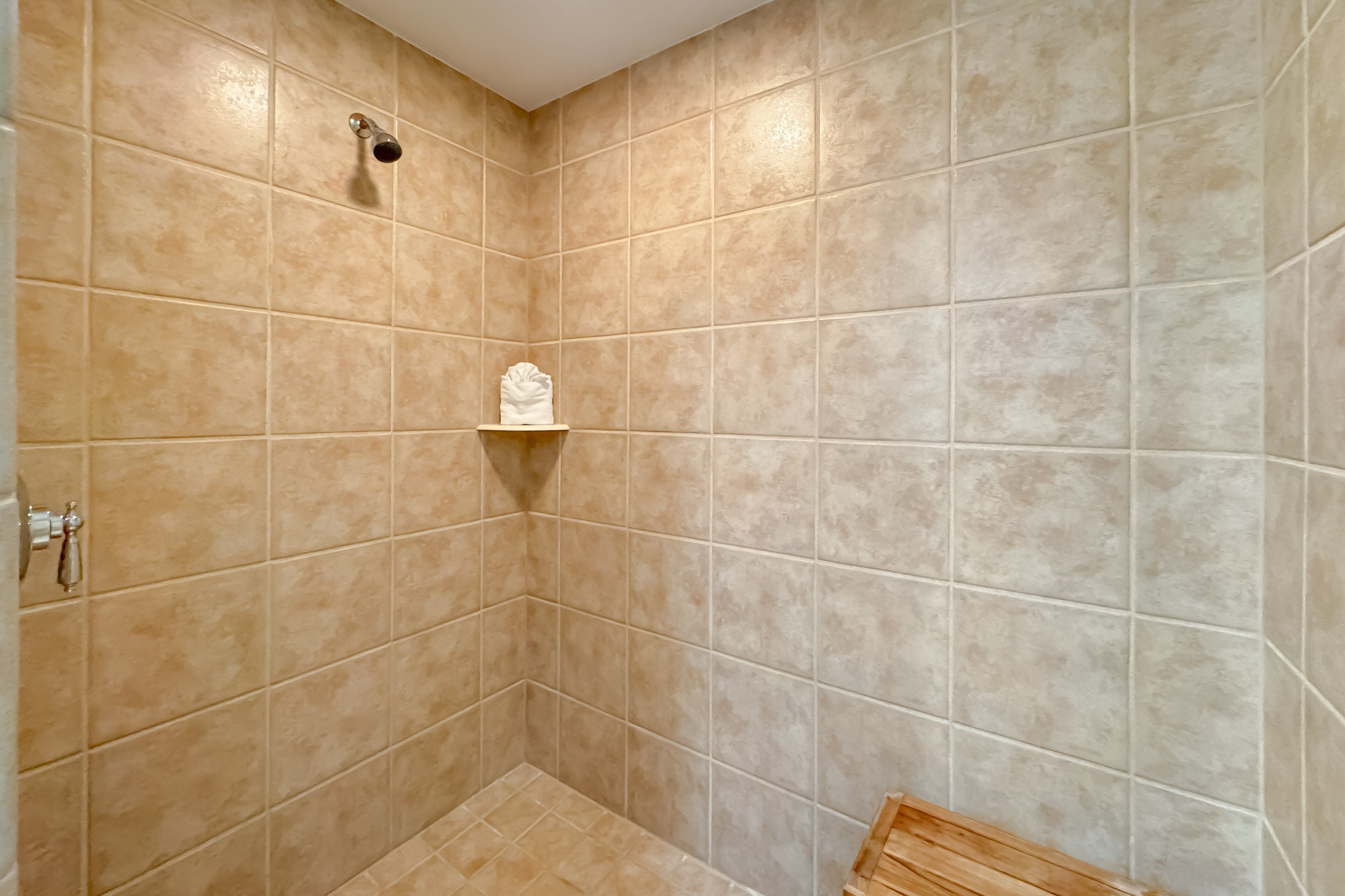 A bathroom with beige tiles, a showerhead, and a towel rack.