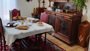 A dining area with a table set for a meal, a hanging plant, a wooden cabinet, and a wall-mounted clock. - Chambre Bleue Guest Room with Shared Terrace, Garden, and Wi-Fi (Saint-Avertin)