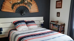 A bed with a striped bedspread, a wooden headboard, a wall-mounted fan, and a small bedside table with a lamp. - Chambre Bleue Guest Room with Shared Terrace, Garden, and Wi-Fi (Saint-Avertin)