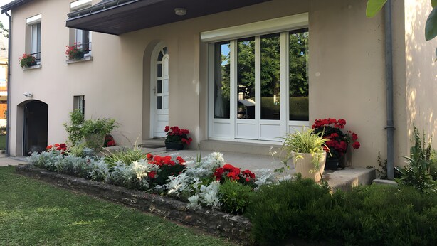 A modern building with a flat roof, large windows, and a well-maintained garden with red and white flowers. - Chambre Bleue Guest Room with Shared Terrace, Garden, and Wi-Fi (Saint-Avertin)