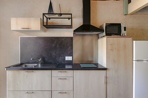 A kitchen with a black countertop, wooden cabinets, a stainless steel sink, and a microwave.