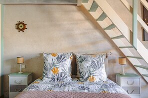 A bedroom with a bed, two nightstands, a wall clock, and a staircase.