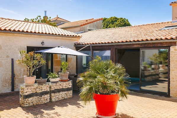 Une cour avec des plantes en pot, un pot rouge et un toit recouvert de tuiles.
