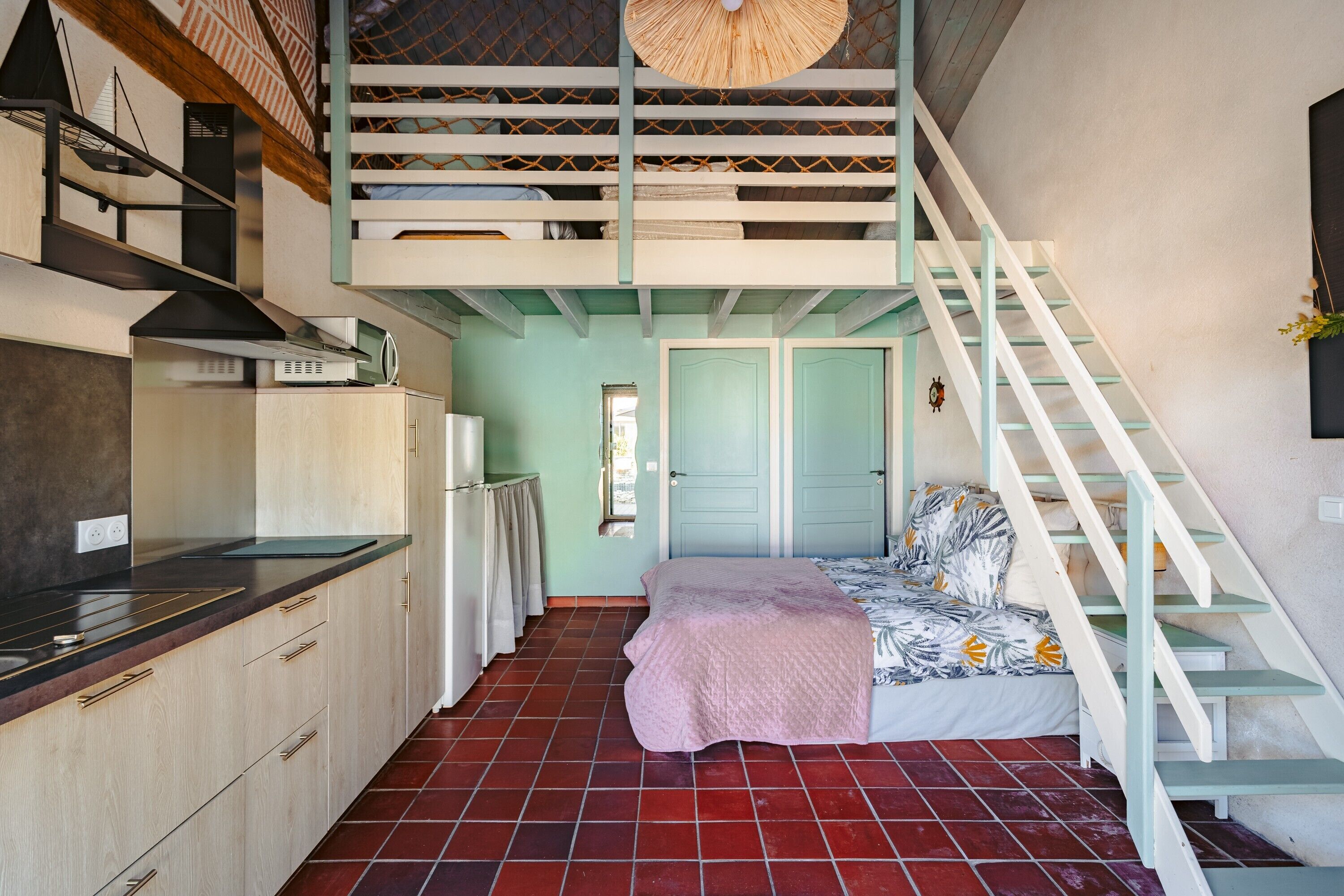 A compact bedroom with a bunk bed, a kitchenette, and a staircase.