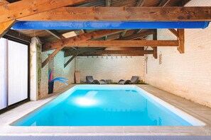 Une piscine intérieure avec un plafond en bois et des murs en briques.