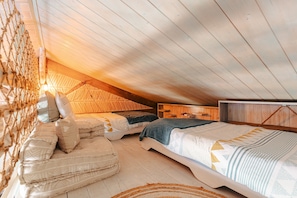 Une chambre confortable situĂ©e dans les combles, avec un plafond en pente, des poutres en bois, un hamac et un lit recouvert dâune literie Ă motifs.