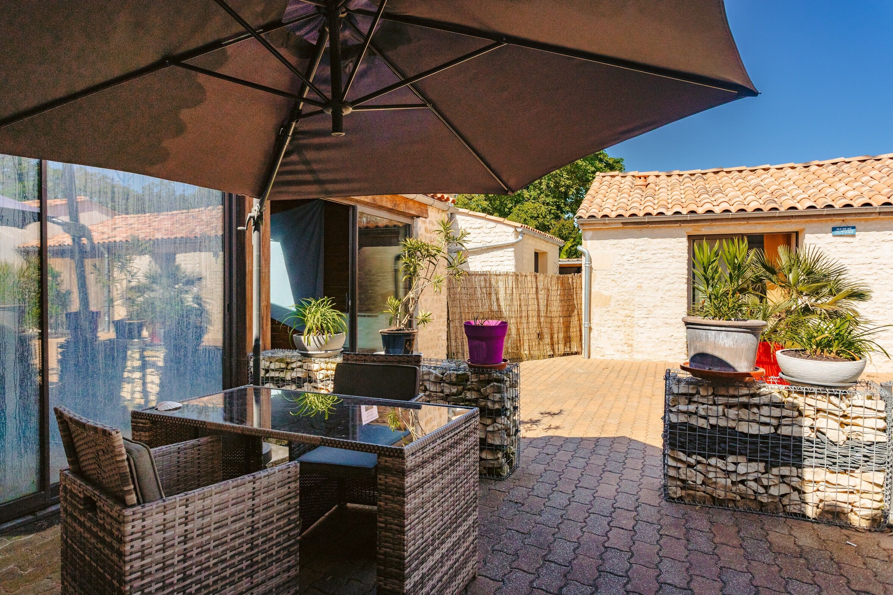 An outdoor patio with wicker furniture, a glass table, and potted plants.