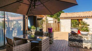 An outdoor patio with wicker furniture, a glass table, and potted plants.