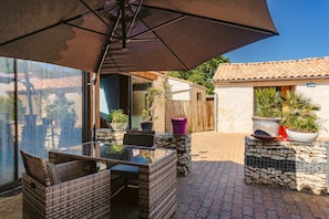 Une terrasse extérieure avec des meubles en osier, une table en verre et des plantes en pot.