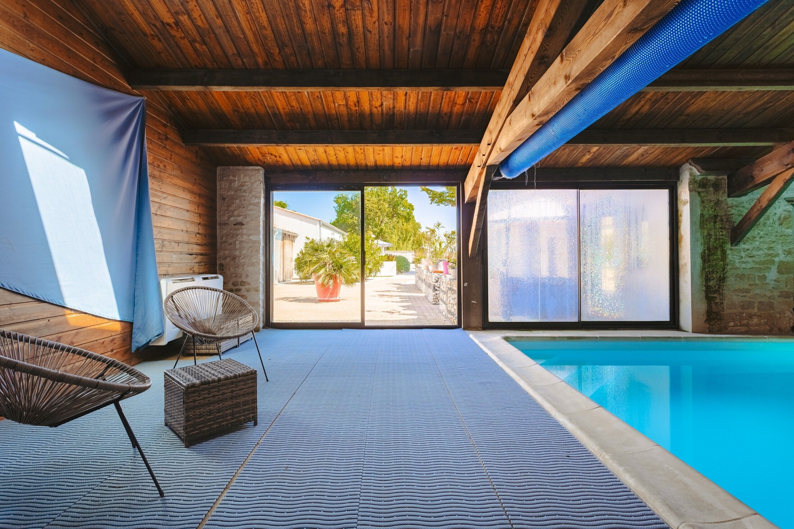 Zona de piscina con techo de madera, una silla de mimbre y vistas al exterior.