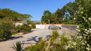A gravel driveway leading to a parked car, surrounded by greenery and a stone wall.