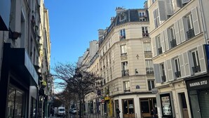 Una calle urbana estrecha flanqueada por edificios, con bicicletas estacionadas a lo largo de la acera, y un cielo azul despejado.