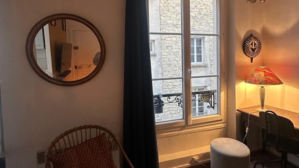 Una habitación con un ventanal grande, una silla, una mesita, una lámpara y un espejo.