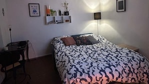 Un dormitorio con cama, escritorio, silla, lámpara de pie y decoración en las paredes.