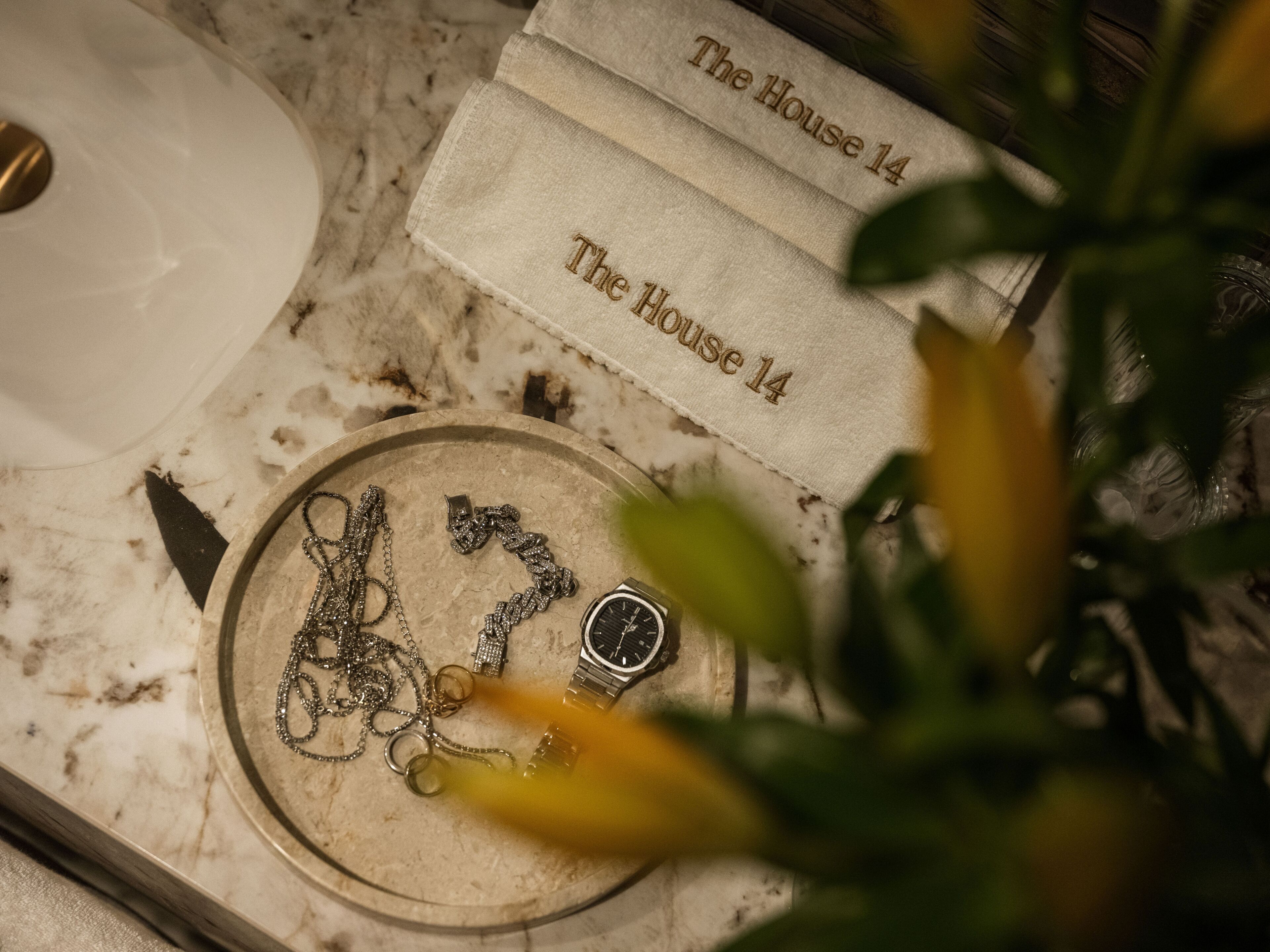 A marble surface with a watch, jewelry, and a cloth with 'The House 14' embroidered.