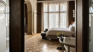 Habitación de hotel con cama, una mesa redonda, una silla, ventana con cortinas y piso estampado.