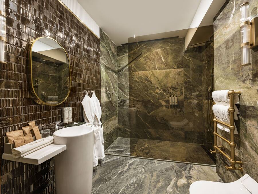 Een moderne badkamer met een douche van marmer, een ronde spiegel en een witte wastafel.