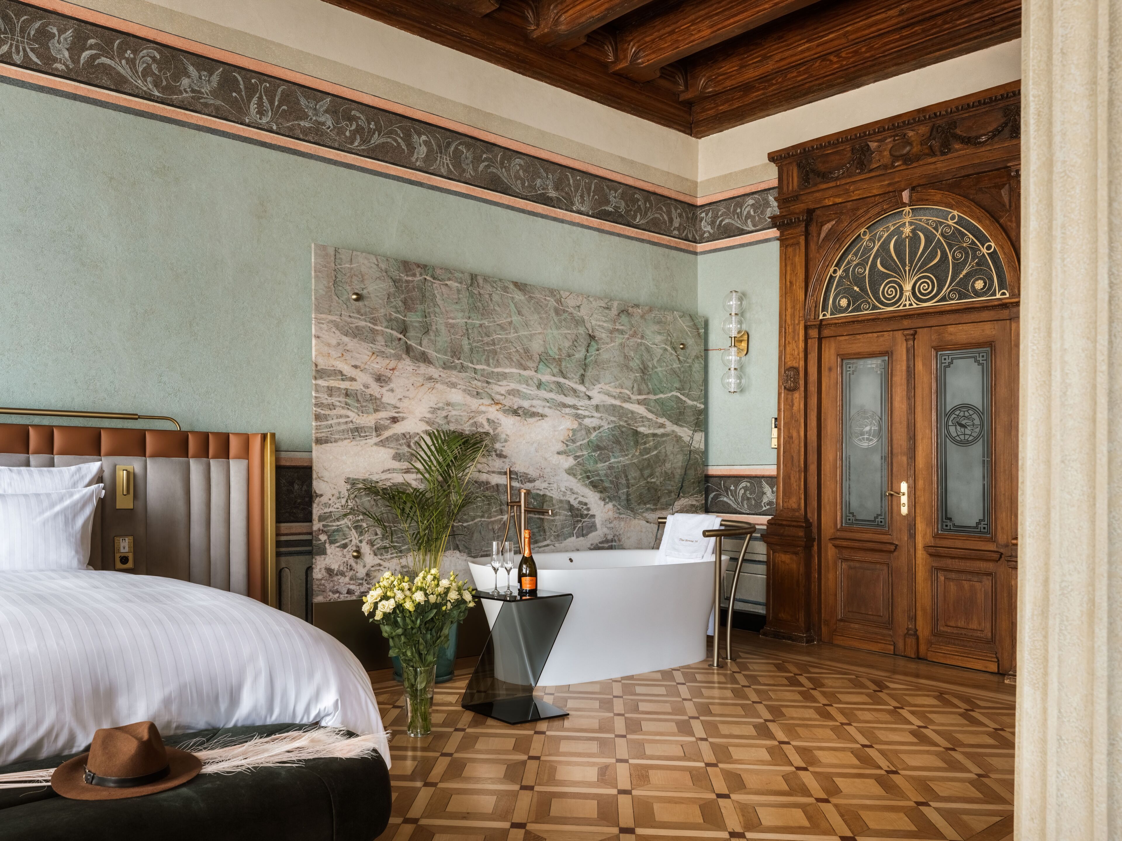 A bedroom with a bed, a nightstand, a vase of flowers, a bottle, and a bathtub.