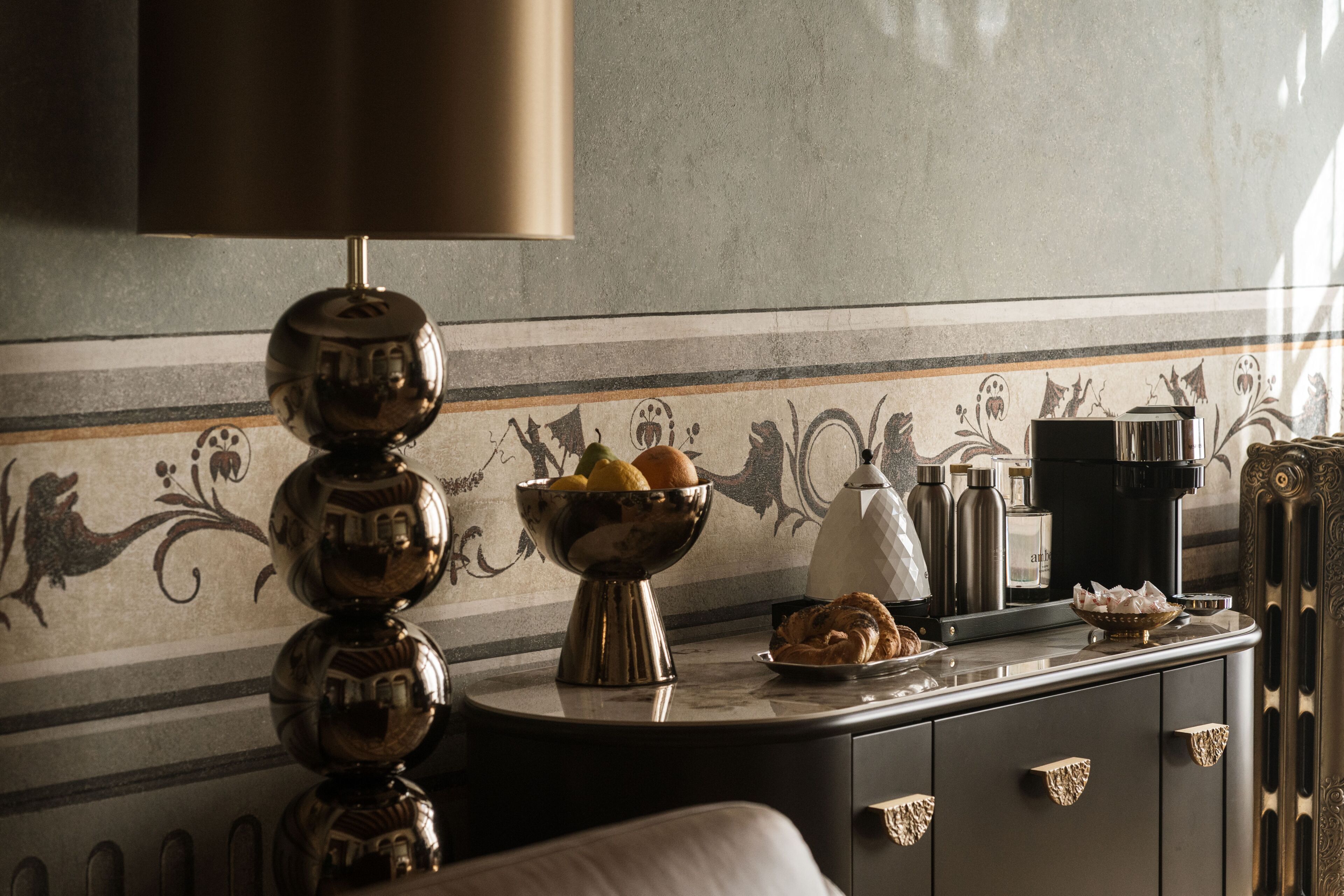 A dining area with a marble countertop, a decorative bowl of fruit, a coffee maker, and a patterned wall.
