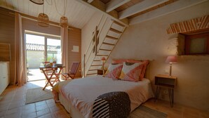 Een slaapkamer met een bed, een stoel, een tafel, een lamp, een raam en een trap.