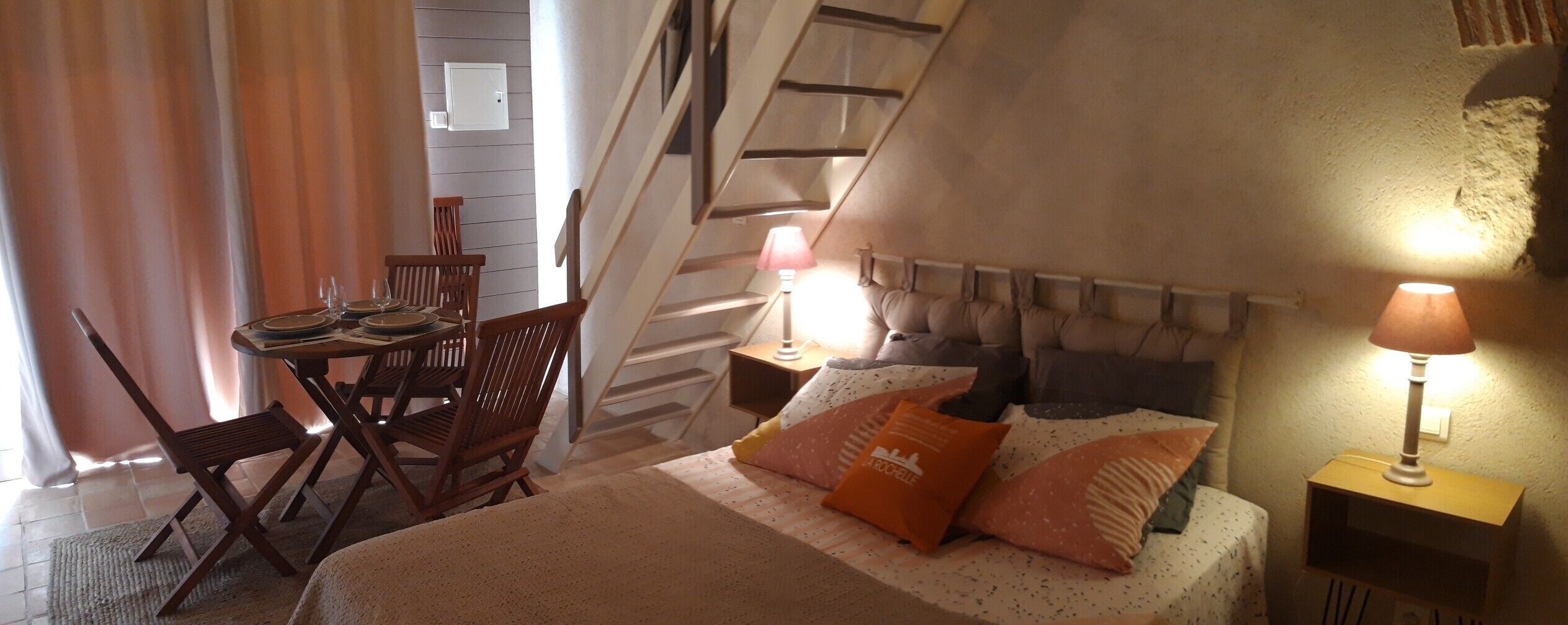 Een slaapkamer met een bed, nachtkastje, lamp, stoel, tafel en een trap.