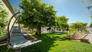 Een gazon met een lounge stoel, bomen en een kleine tuin.