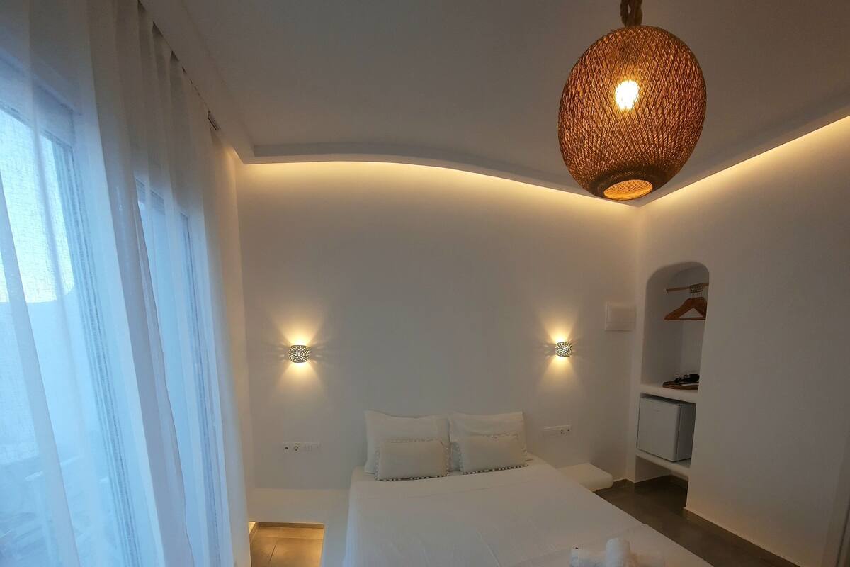 Un dormitorio con una cama grande, dos luces fijadas a la pared, una lámpara colgante y un zapatero.