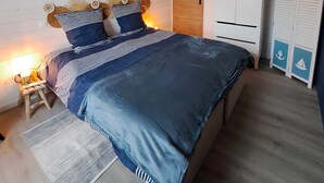 Un dormitorio con cama, lámpara de noche, techo de madera, armario y una puerta.