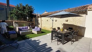 Un patio con mobiliario exterior, una mesa y una zona de barbacoa.
