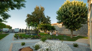 Un jardín con senderos de grava, árboles y un muro de piedra.