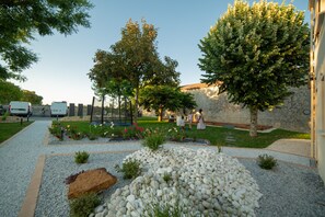 Een tuin met grindpaden, bomen en een stenen muur.