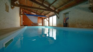 Una piscina interior con vigas de madera, paredes de piedra y vistas a una escalera.