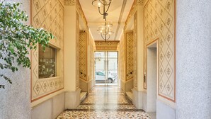 A hallway with patterned walls, a tiled floor, and a chandelier. - Ariosto Living (Milan)