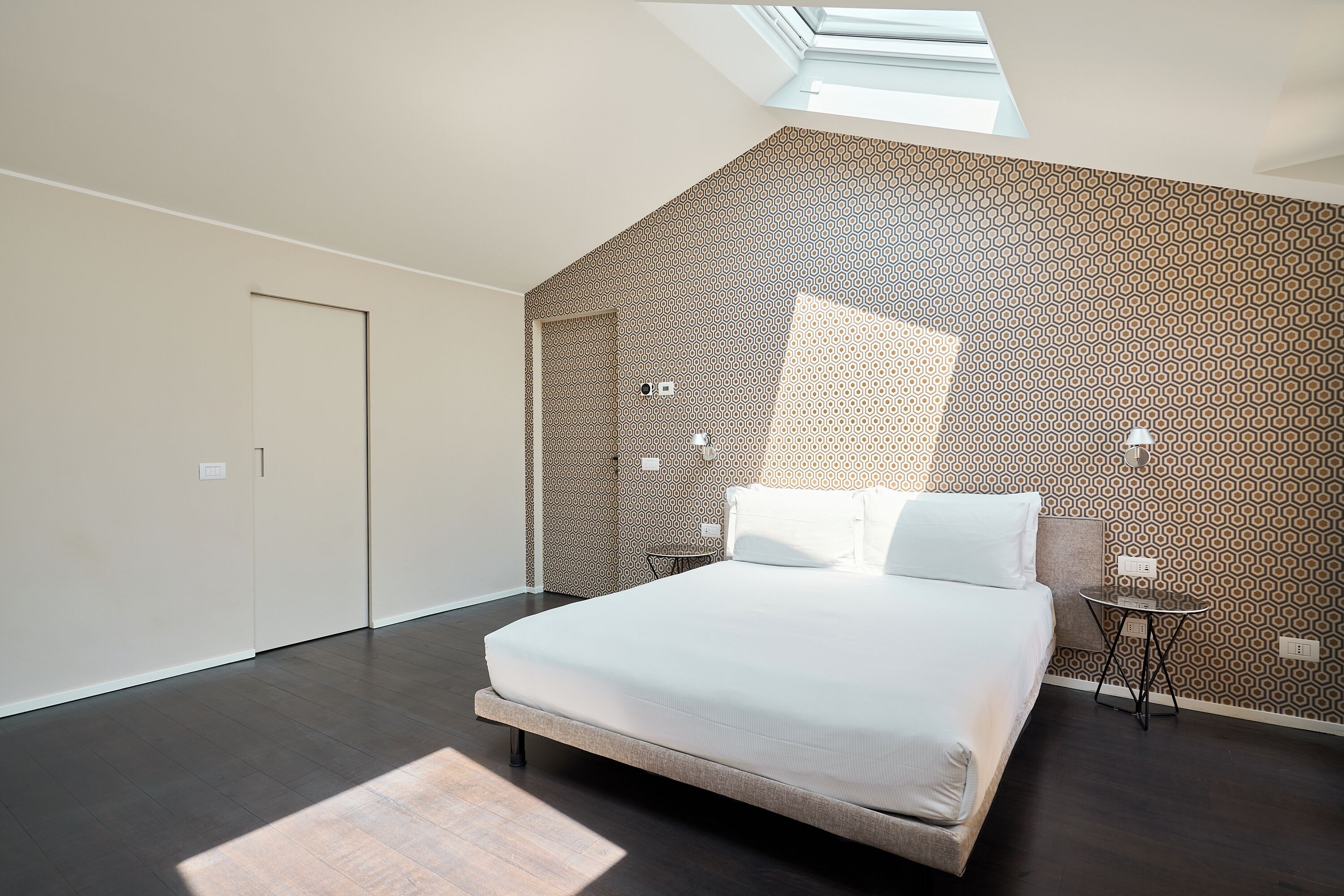 A modern bedroom with a skylight, patterned wallpaper, a bed, and a small table.