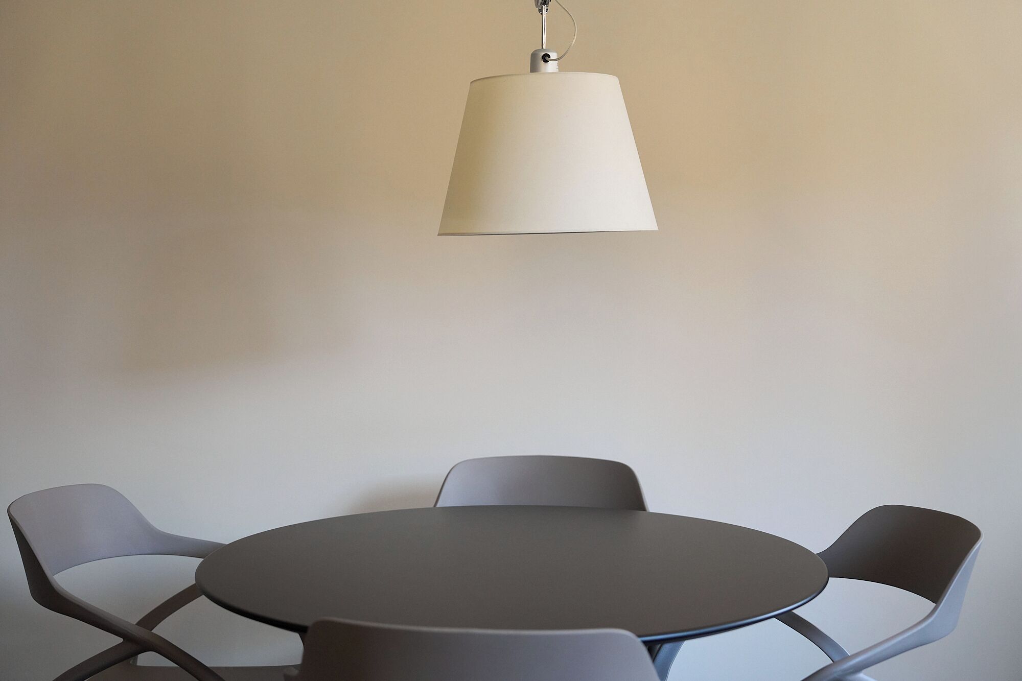 A round table with four chairs, a hanging lamp, and a plain wall.