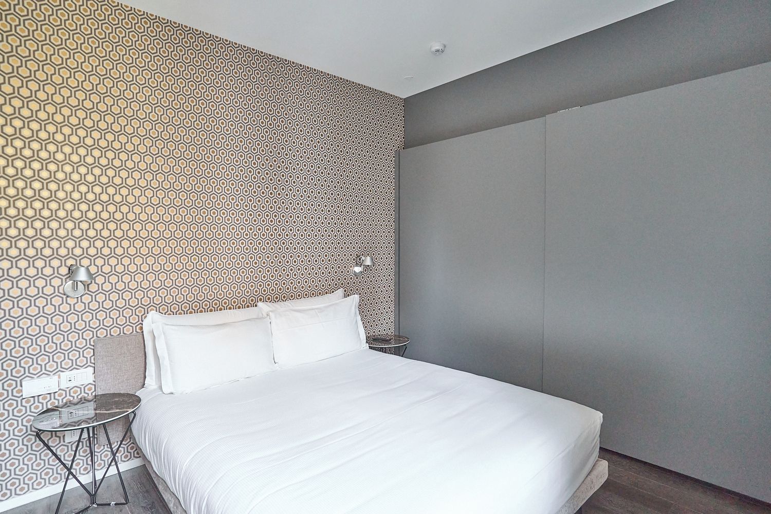 Una habitación de hotel moderna con una cama grande, una mesita redonda pequeña y una pared con diseño.