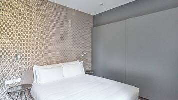 Una habitación de hotel moderna con una cama grande, una mesita redonda pequeña y una pared con diseño.