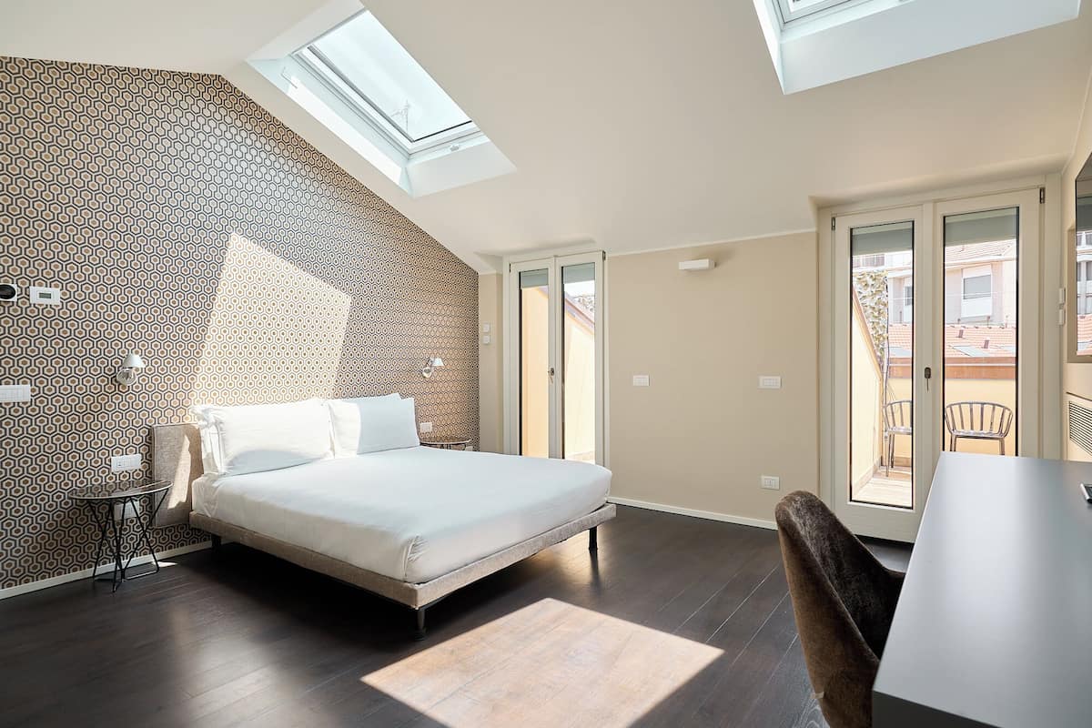 Un dormitorio con cama, tragaluces, balcón y pared con diseño.