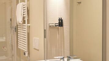 A modern bathroom with a glass-enclosed shower, a white sink with a mirror, and a towel rack.