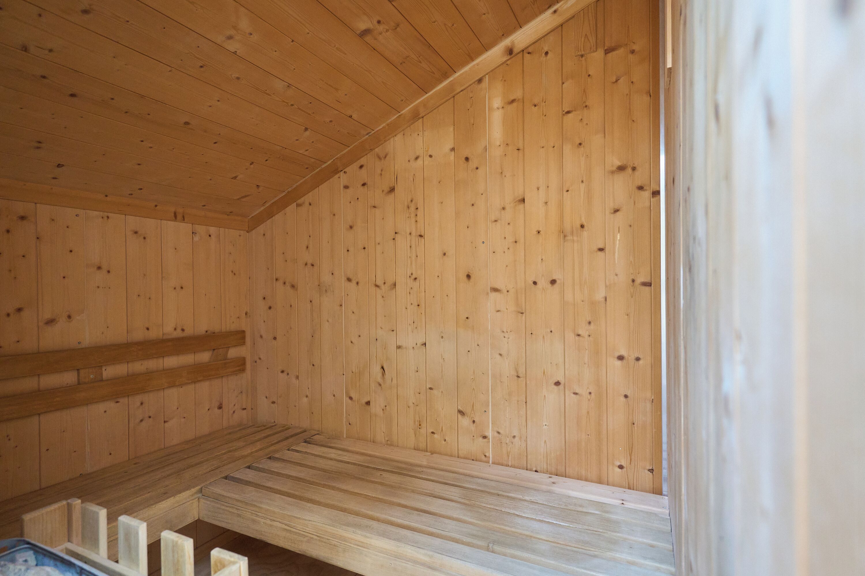 Interior de una cabaña de madera con un banco, paredes de madera y una ventana.