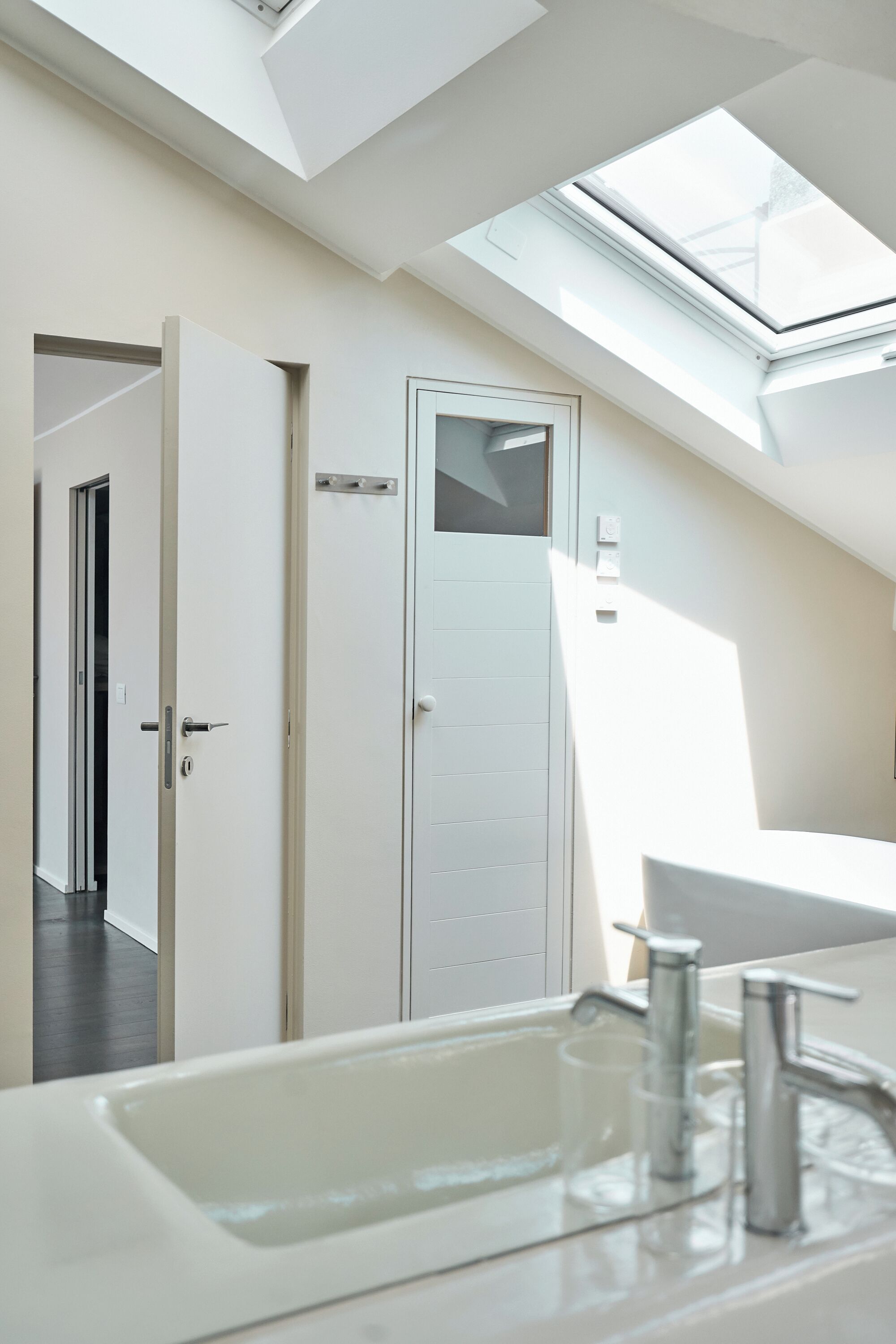 A modern bathroom with a skylight, a white sink, and a door leading to another room.