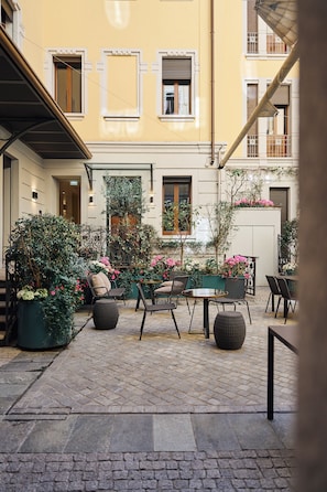 An outdoor seating area with tables and chairs, surrounded by potted plants and flowers.